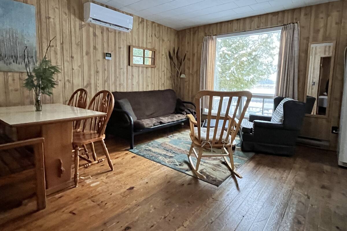 A wooden-paneled room with a dining table, chairs, a sofa, and a rocking chair.