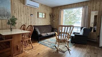 A wooden-paneled room with a dining table, chairs, a sofa, and a rocking chair.