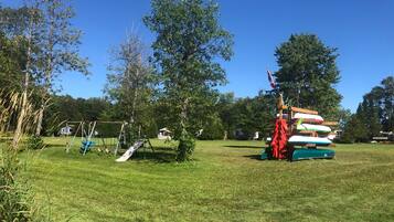 A grassy park with a swing set and a pile of boats.