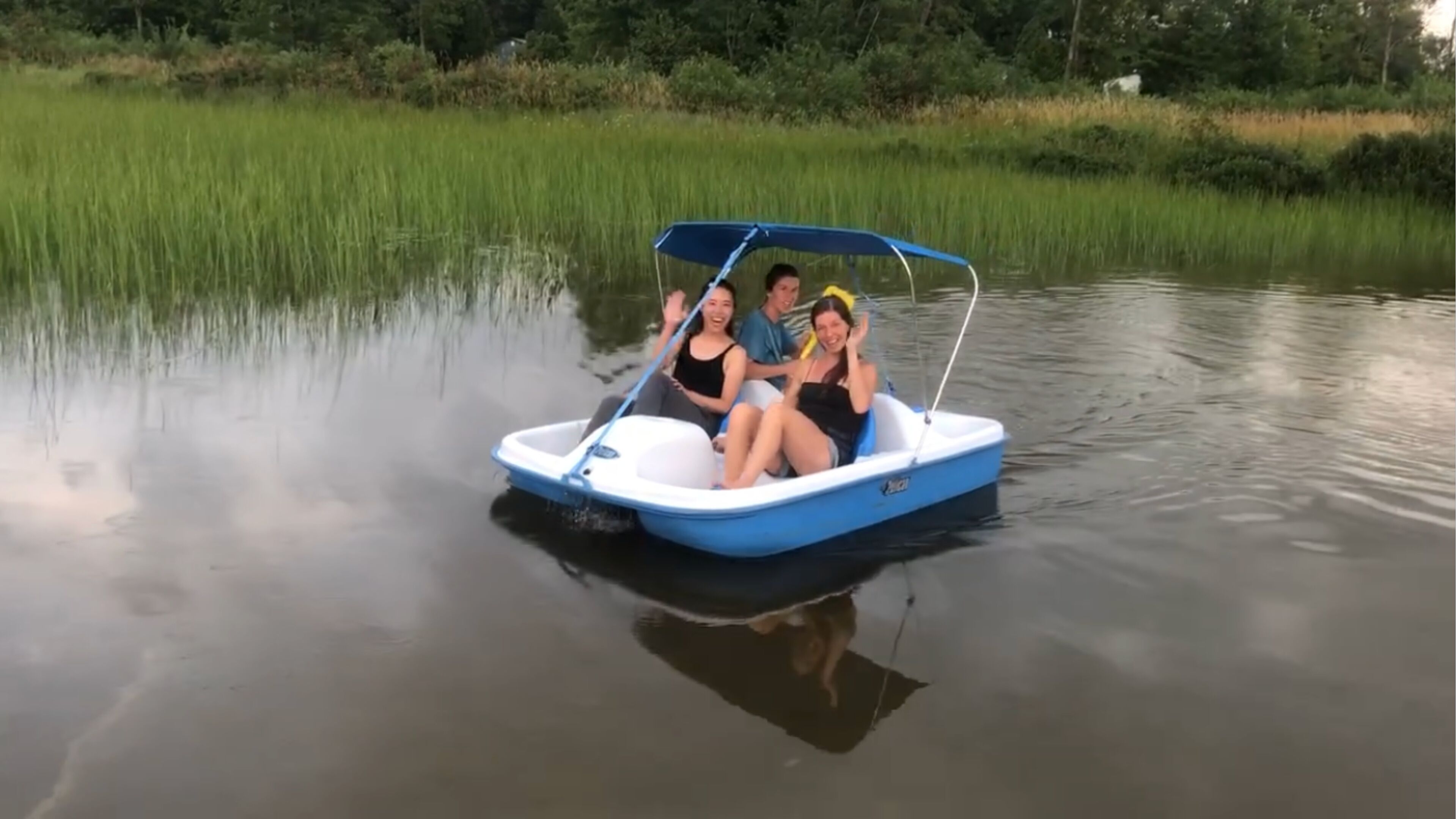 Una piccola barca blu con una tenda da sole, due persone sedute all'interno e acqua calma.