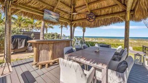 An outdoor deck with a thatched roof, a bar area, and seating. - Oceanfront Cocoa Beach Home | Direct Beach Access | Tiki Bar & Fire Pit (Cocoa Beach)