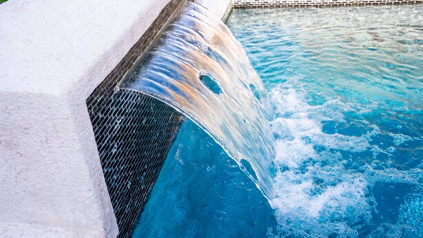 A pool with a waterfall feature, a tiled edge, and a brick pattern at the bottom.
