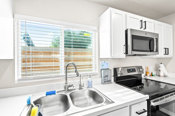 A modern kitchen with stainless steel appliances, white cabinetry, and a window with blinds. - Casa del Sol: Luxury Heatable Pool with Private Guest House (Laredo)