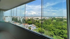 Quarto com grandes janelas do chão ao teto, com vista para a paisagem urbana e áreas verdes.