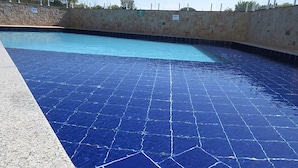 Piscina com chão de azulejos azuis e parede de pedra ao redor.