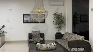 Uma sala de estar moderna com um sofá grande e curvo, um sofá menor e um chaise lounge. Há um lustre grande e ornamentado pendurado no teto.