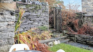 A stone wall with a metal gate, a grassy area, and a white plastic table and chair.