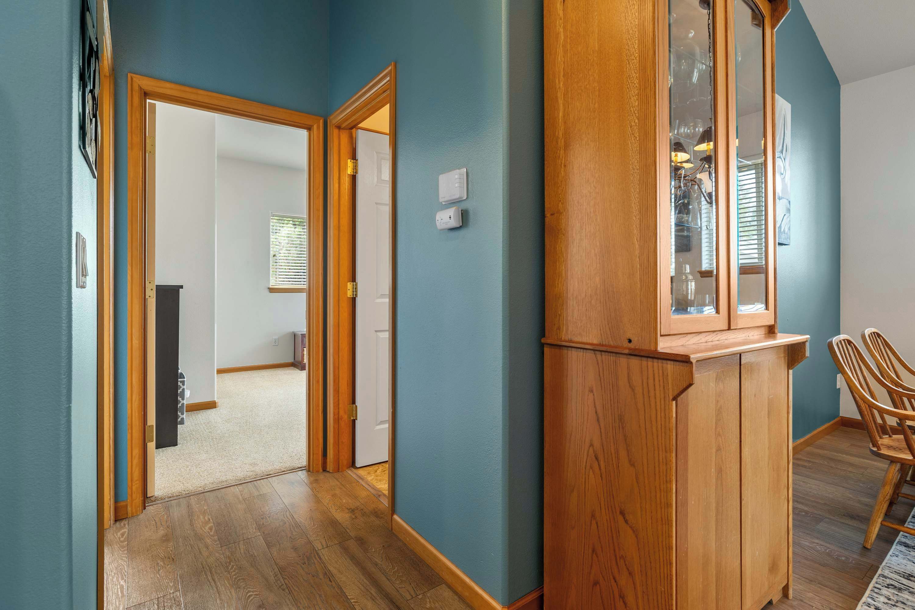 A hallway with wooden flooring, a wooden cabinet with glass doors, and a door leading to another room.