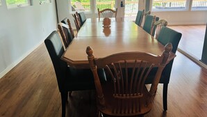Un grande tavolo da pranzo con sedie in legno, ampie finestre che si affacciano sul verde e un patio esterno in legno.