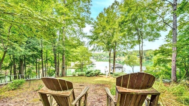 Due poltrone in legno di stile Adirondack rivolte verso un lago, con una casa sullo sfondo.
