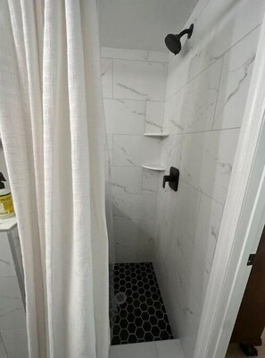 Shower area features a bathtub and towel hooks.