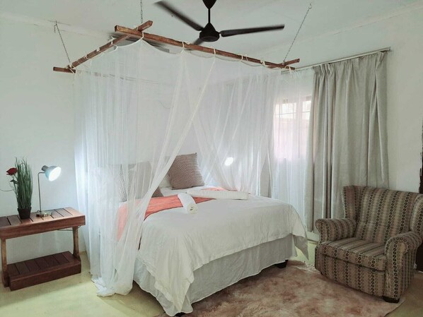 A bedroom with a bed under a canopy, a chair, a bedside table with a lamp, and a window with curtains. - The Sky Safari Lodge - Hoedspruit (Hoedspruit)