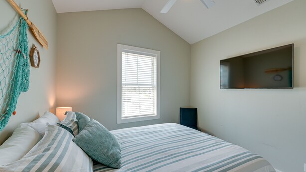 A bedroom with a bed, a window with blinds, a hanging net, and a mounted TV.