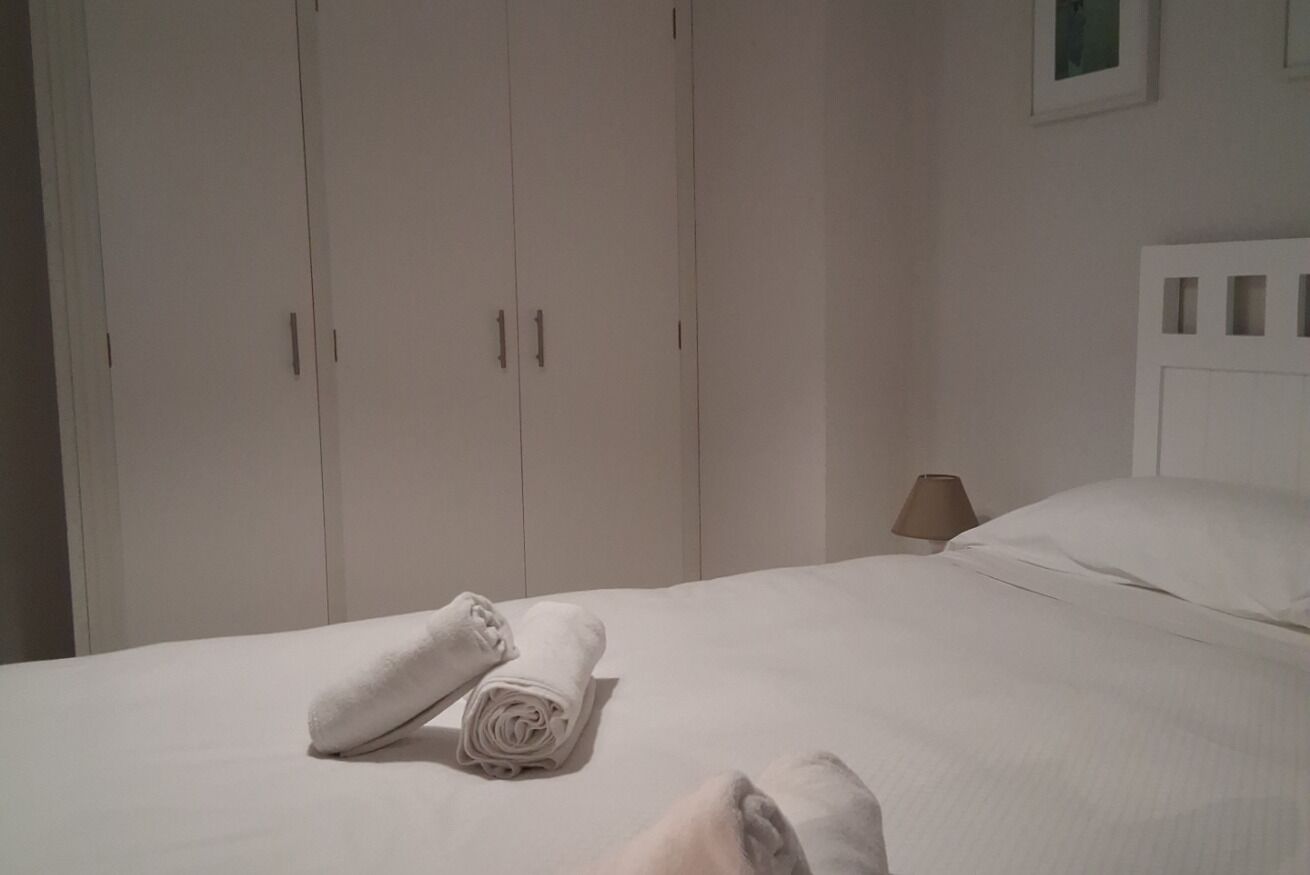 A neatly made bed with rolled towels, a bedside lamp, and a white headboard.