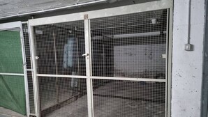 Een metalen poort met het nummer '12' erop, bevestigd aan een gebouw met een betonnen vloer.
