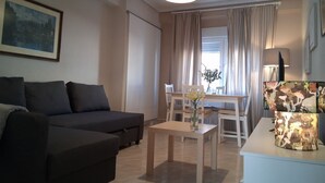 Een woonkamer met een bank, een tafel met een bloevas en een lamp.