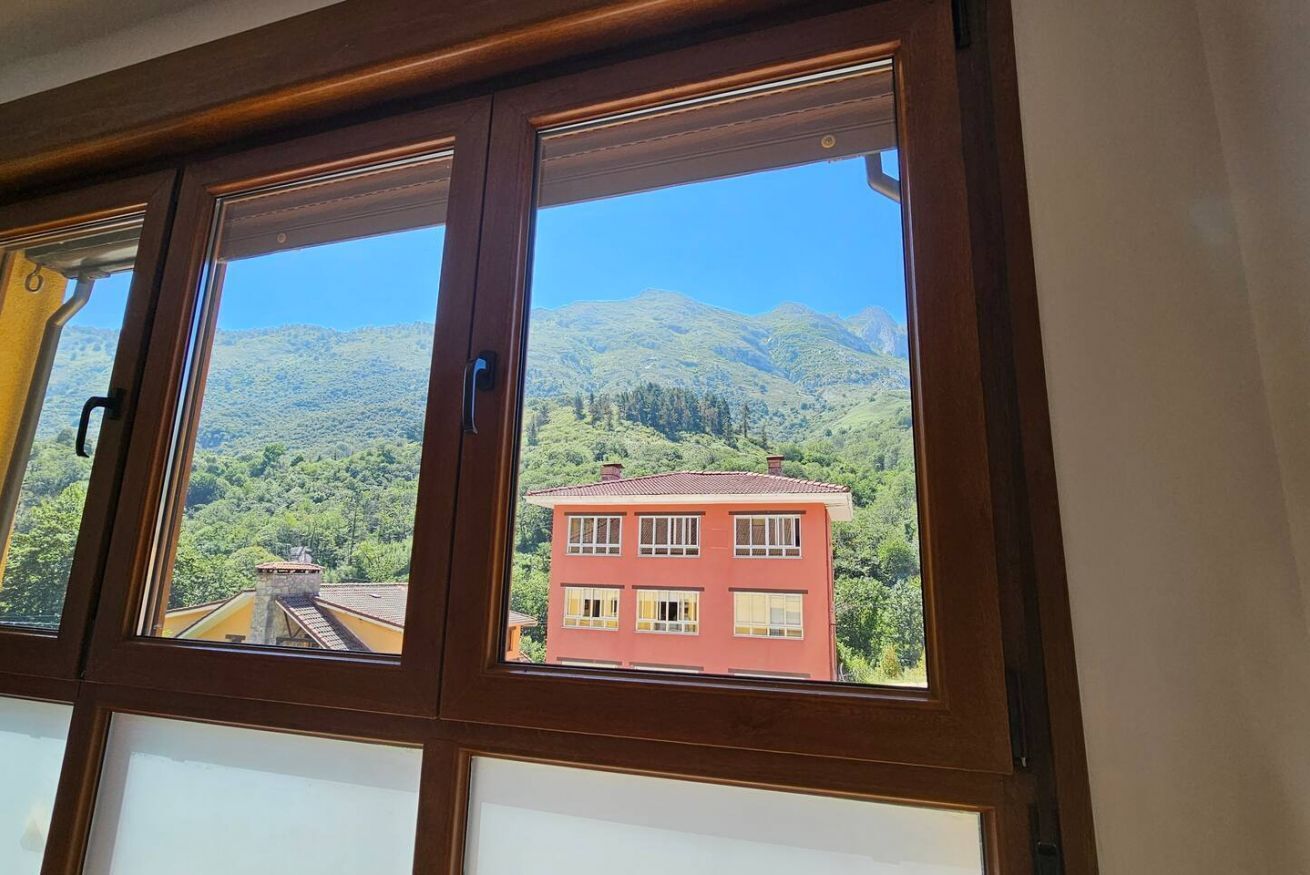Una finestra amb vista a un edifici vermell i muntanyes.