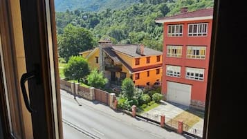 Vista a través de una ventana que muestra una calle con edificios, cielo despejado y un paisaje montañoso.