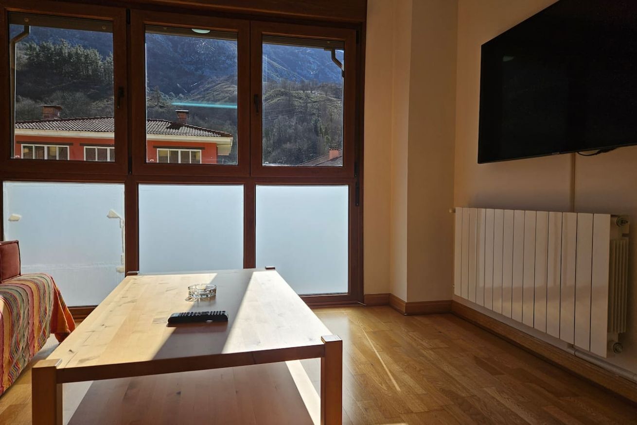 Une pièce avec une grande fenêtre, une table en bois, un lit et un téléviseur.