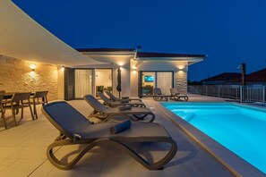 A modern outdoor pool area with lounge chairs and a stone wall. - Villa Paloma with pool (Sukošan)