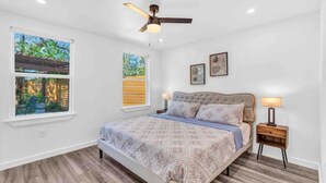 Une chambre à coucher avec un lit, un ventilateur de plafond, deux fenêtres et une table de chevet.