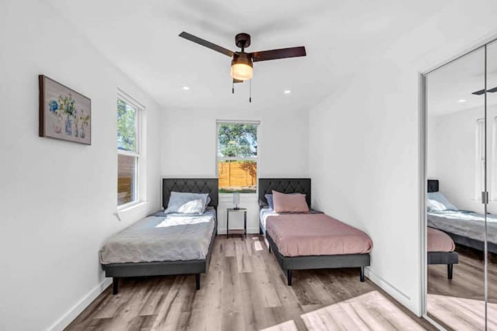 A bedroom with two beds, a ceiling fan, and a window with a view of trees.