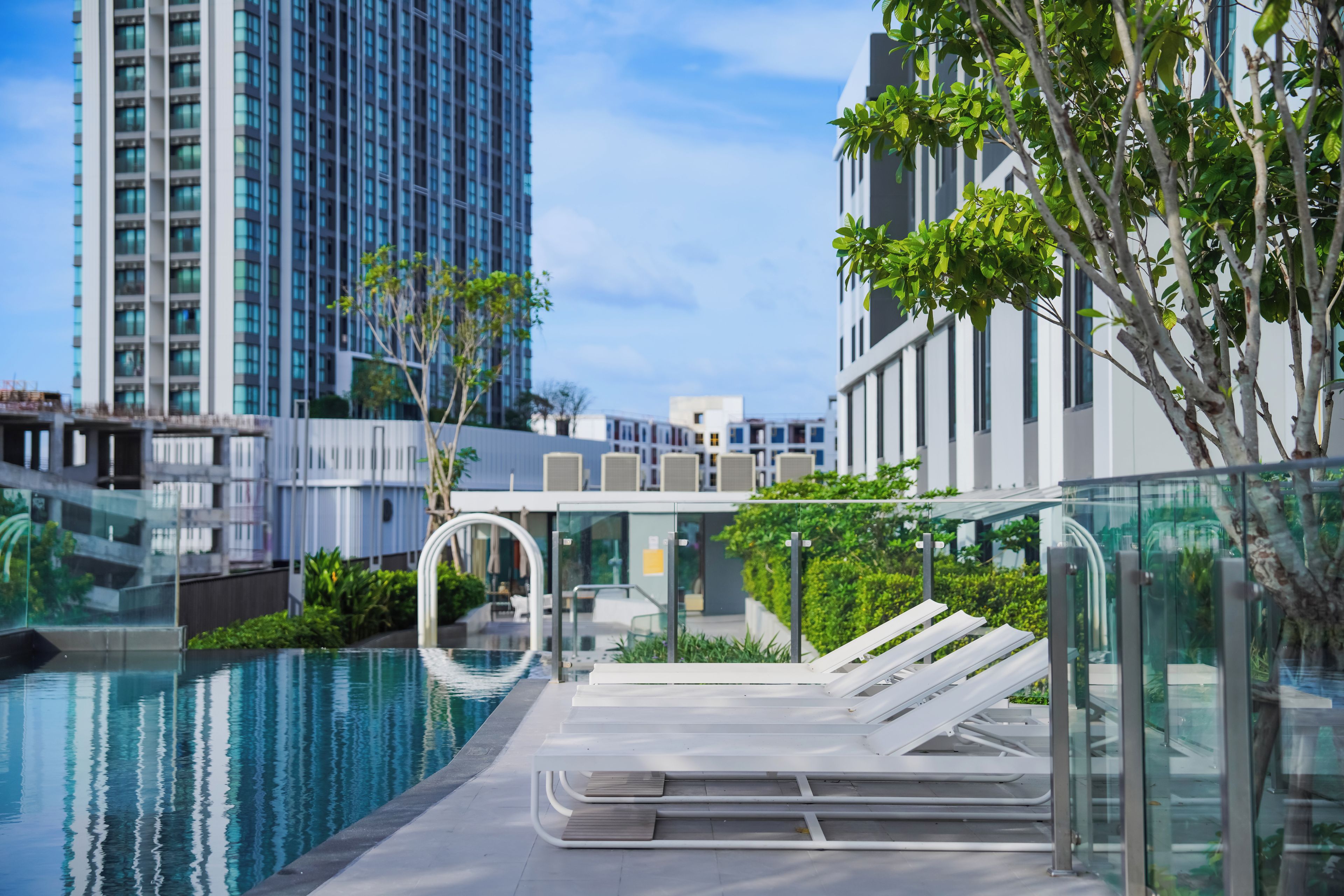 A modern swimming pool with lounge chairs, surrounded by buildings and greenery.