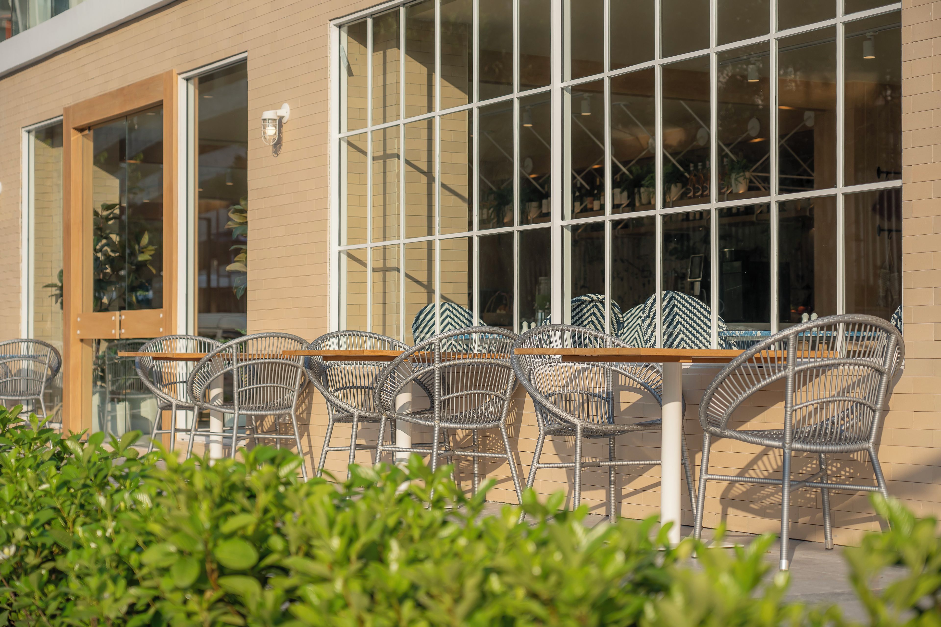 An outdoor seating area with metal chairs and tables, a brick building facade, and a window with a view into the interior.