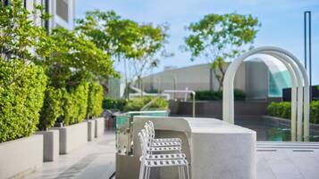 A modern outdoor seating area with a pool, greenery, and a contemporary building in the background.