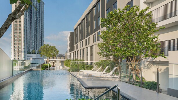 A modern building with a swimming pool, lounge chairs, and a tree in the foreground. - Holiday Inn Express Rayong by IHG (Rayong)