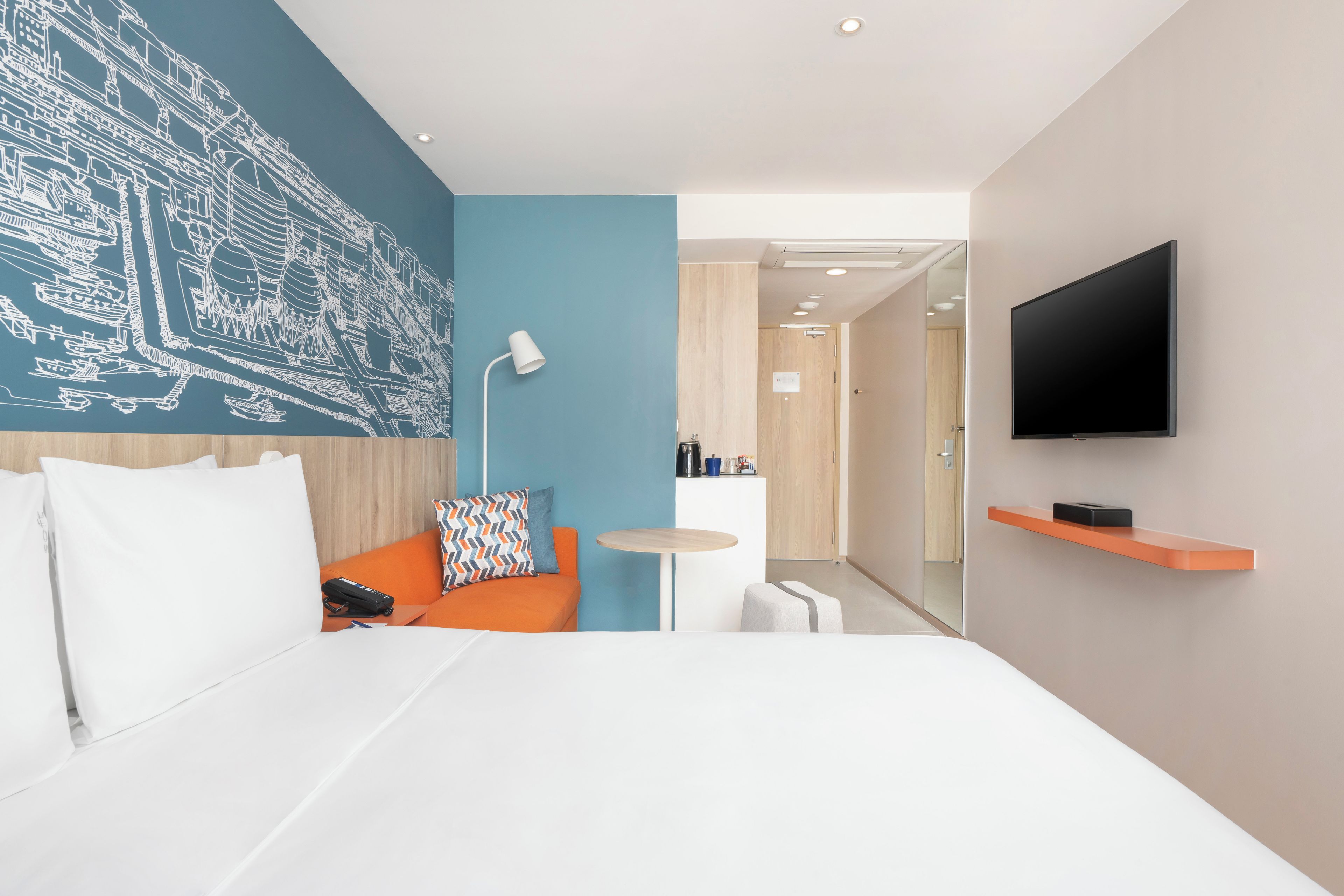 Une chambre d’hôtel moderne avec un grand lit, un petit canapé, un bureau, une télévision et une fresque murale.