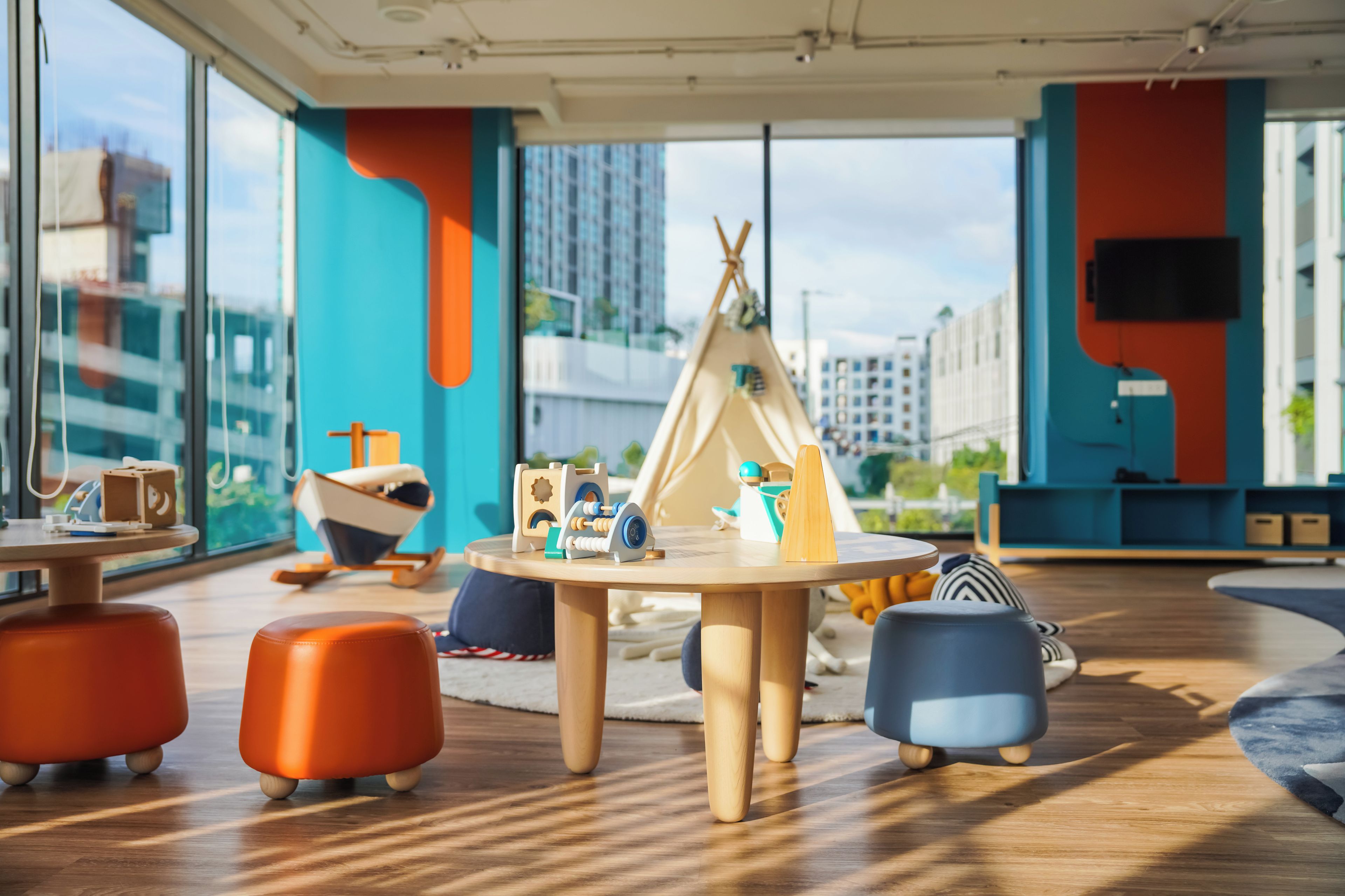 A modern children's play area with a round table, colorful seating, and a teepee play structure.