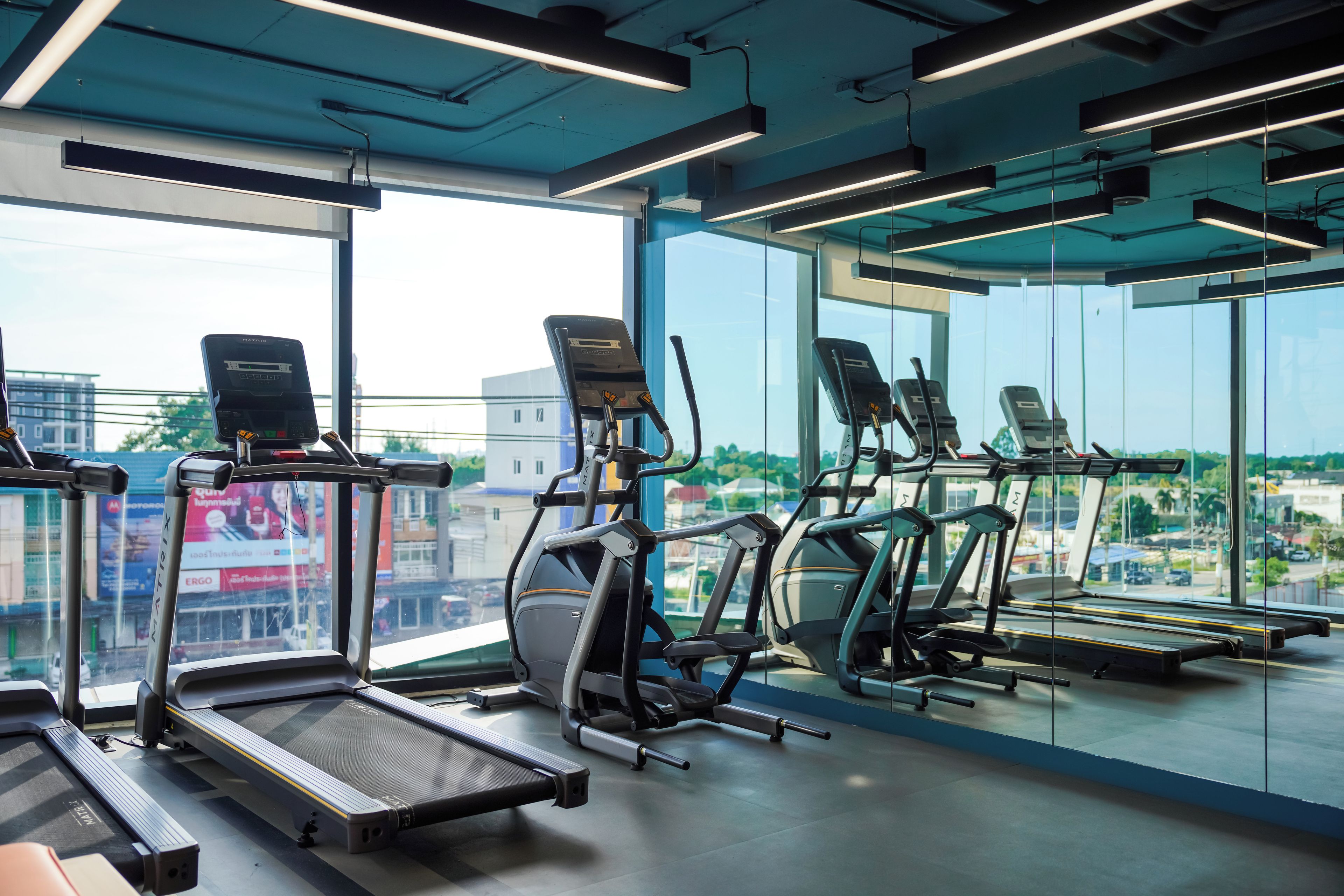 Un gimnasio con cintas de correr y bicicletas estáticas, ventanas amplias y vistas a la ciudad.