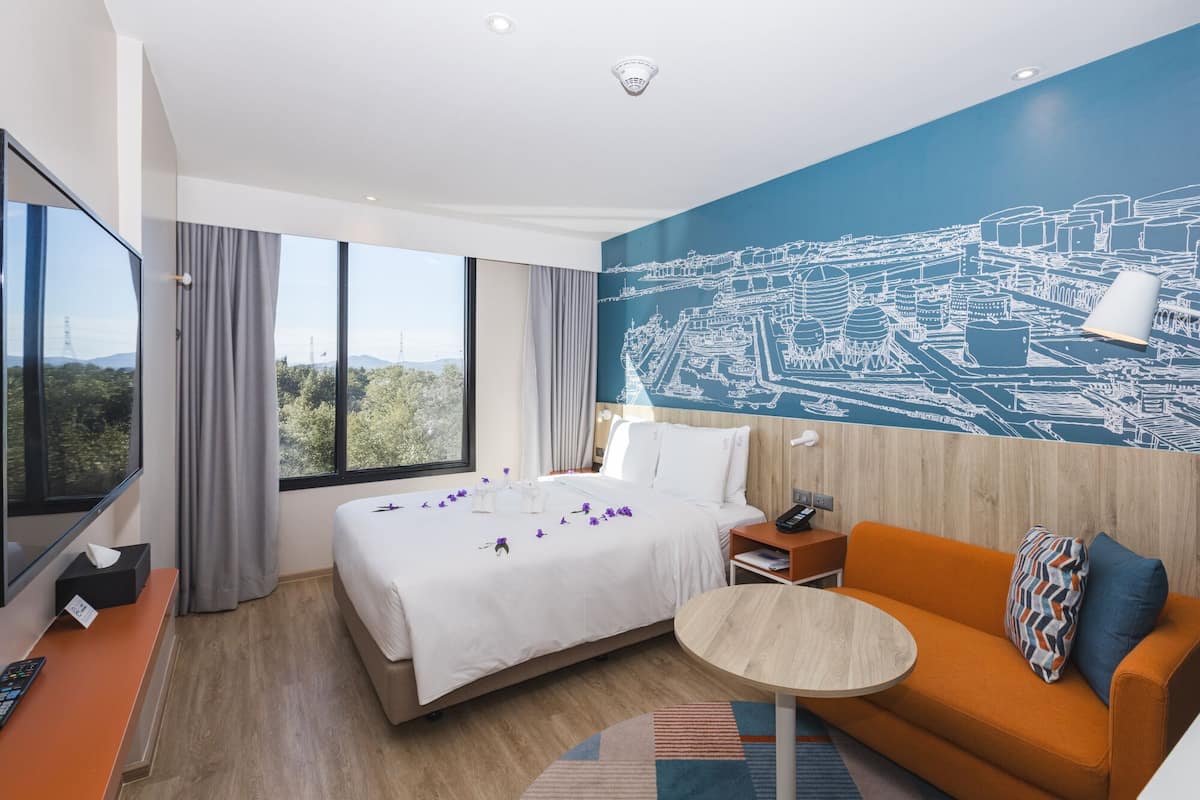 A hotel room with a large bed, a sofa, a small table, a TV, and a cityscape mural on the wall.