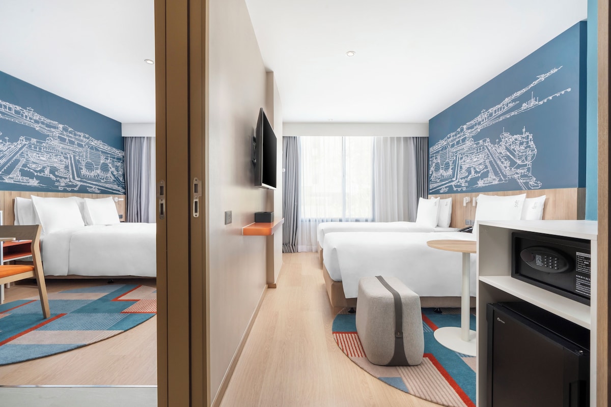 Een hotelkamer met twee bedden, een flatscreen televisie, een bureau, een magnetron en een groot raam met gordijnen.