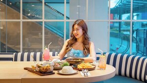 A person dining at a table with various dishes and drinks, large windows with a view of an escalator, and a modern interior design. - Holiday Inn Express Rayong by IHG (Rayong)