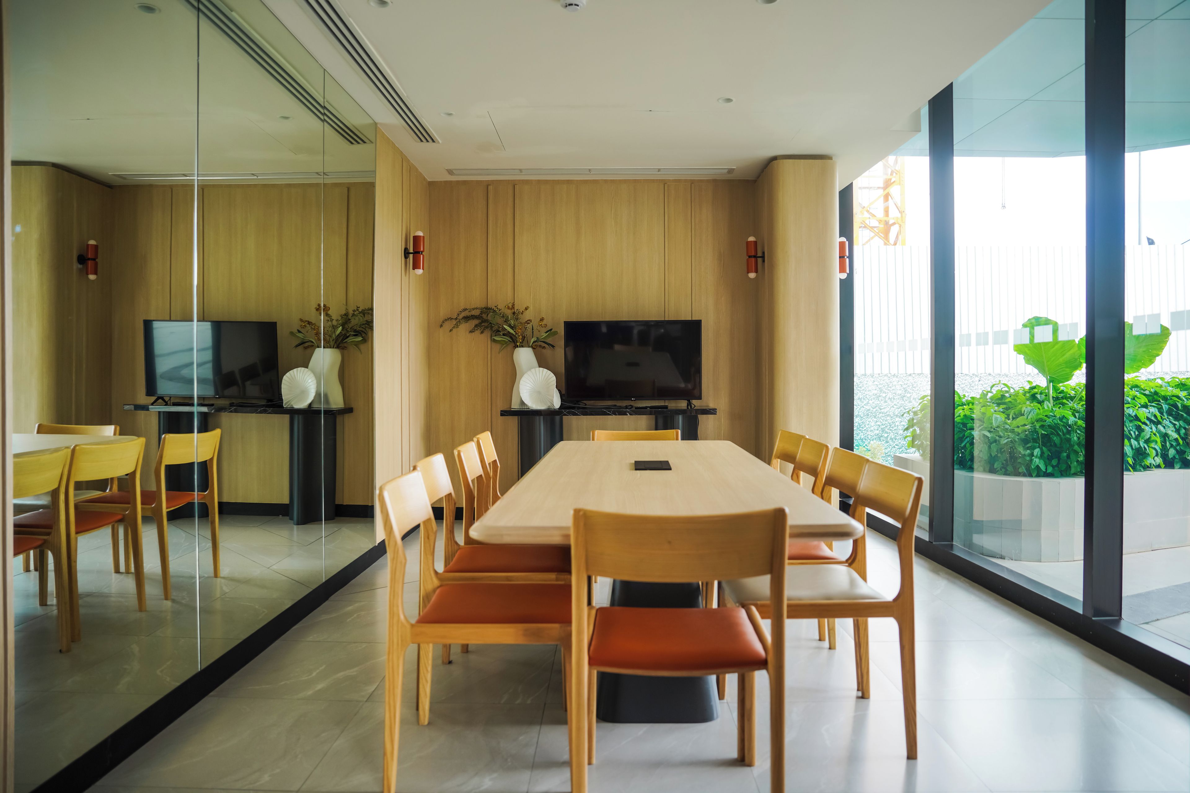 A modern conference room with a long table, chairs, a television, and a glass partition.