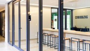 Un espacio de coworking moderno con divisiones de vidrio, una zona de recepción y varios taburetes.