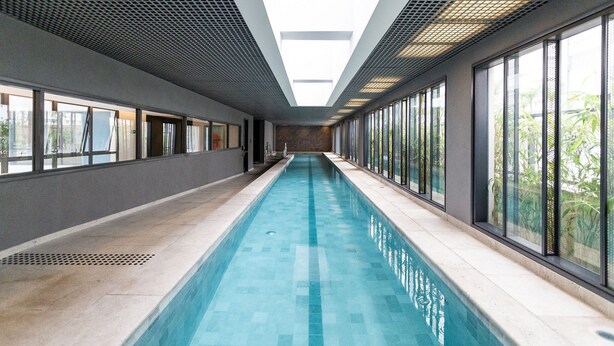 Una piscina interior extensa con techo de tragaluces y grandes ventanales a ambos lados.
