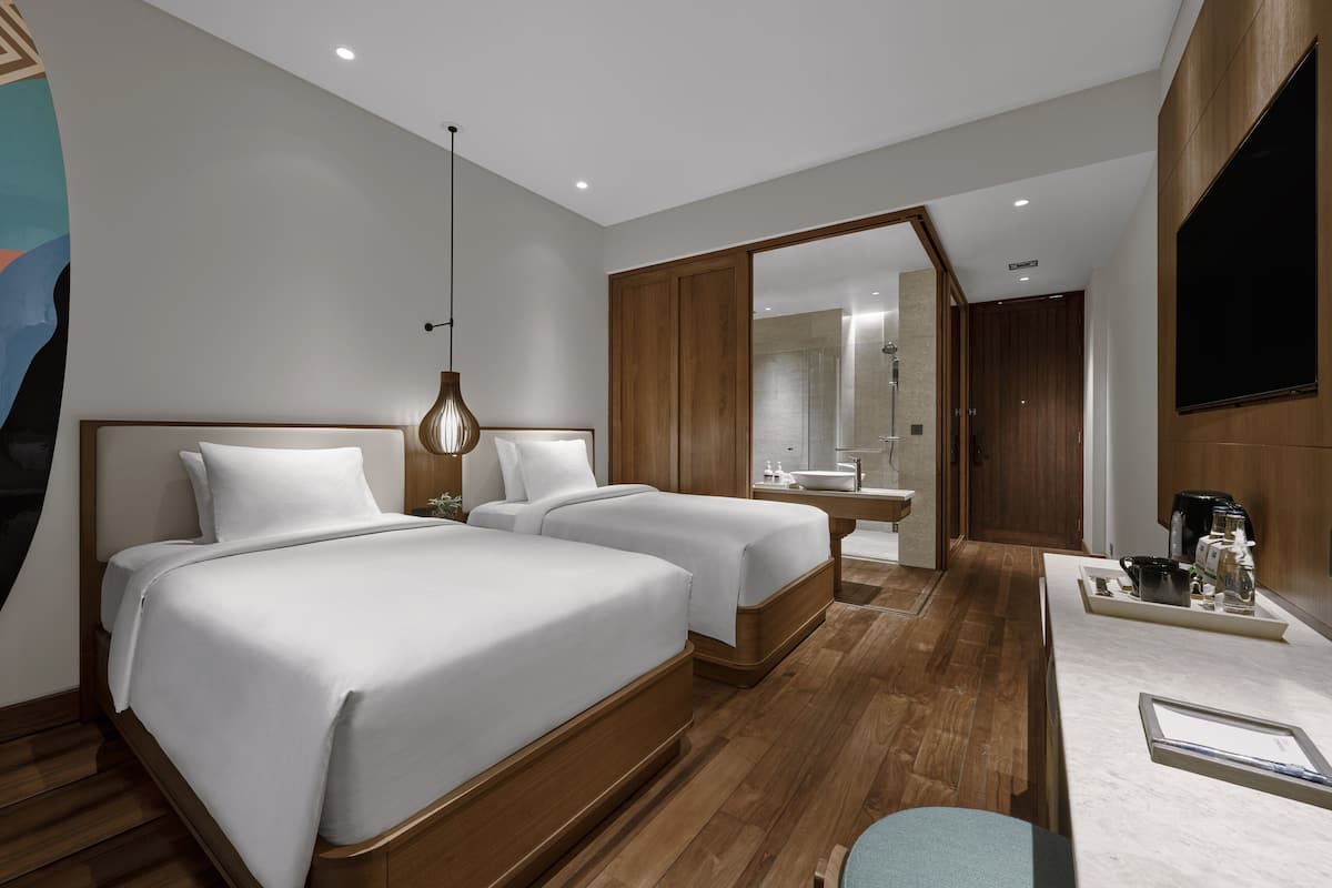Une chambre d’hôtel avec deux lits, un bureau, un miroir et un espace douche.
