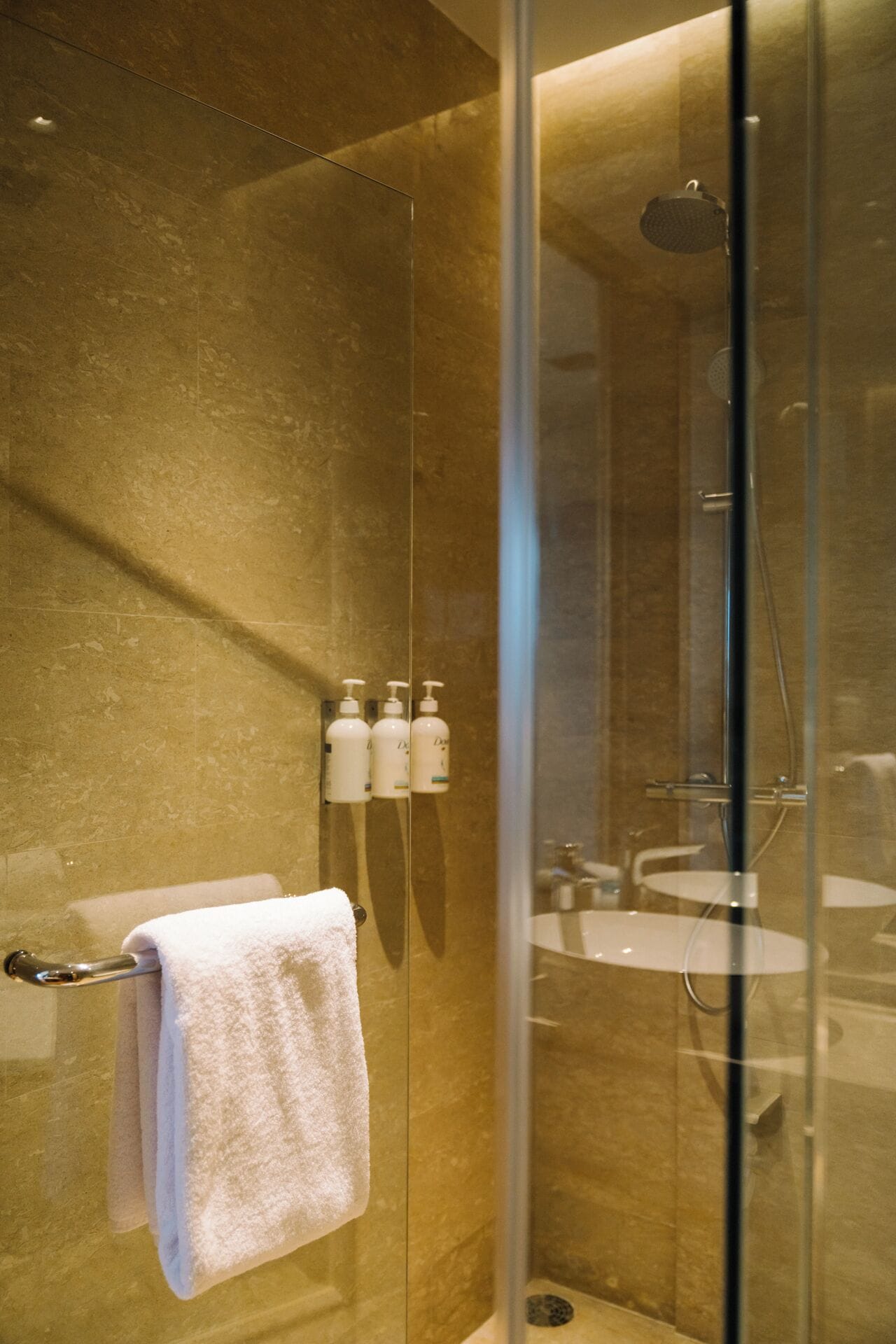 A glass-enclosed shower with a handheld showerhead, a glass door, and a towel rack with a white towel.
