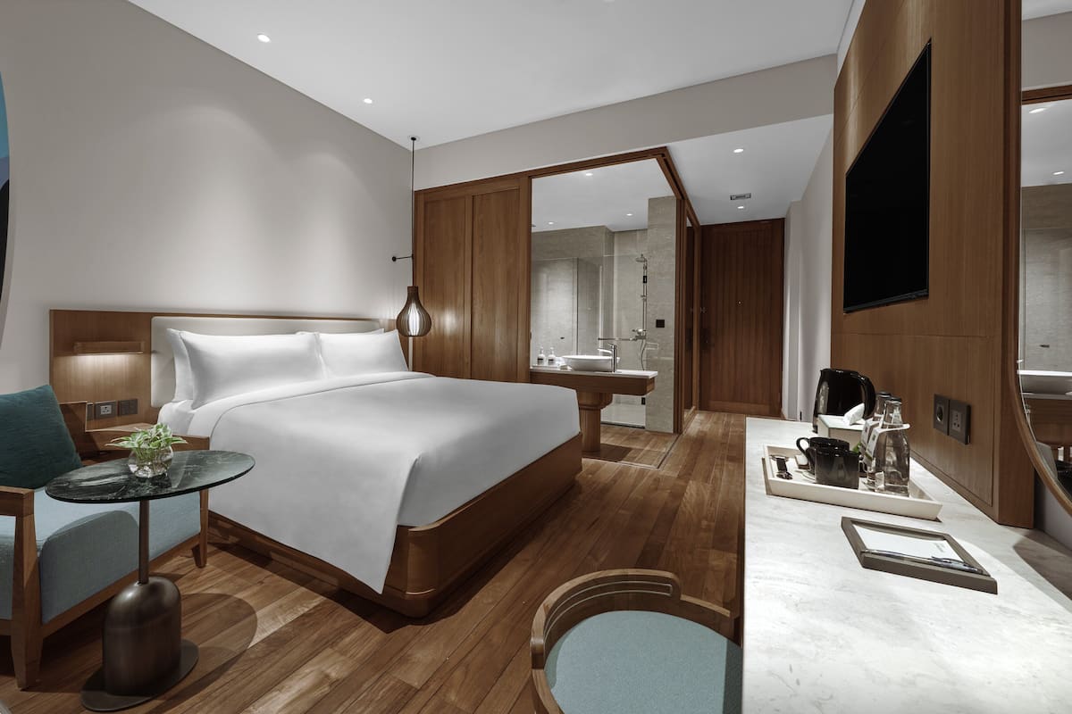 Une chambre d’hôtel moderne dotée d’un grand lit, d’un coin salon avec une table et des chaises, d’une salle de bain avec douche et lavabo, et d’un téléviseur fixé au mur.