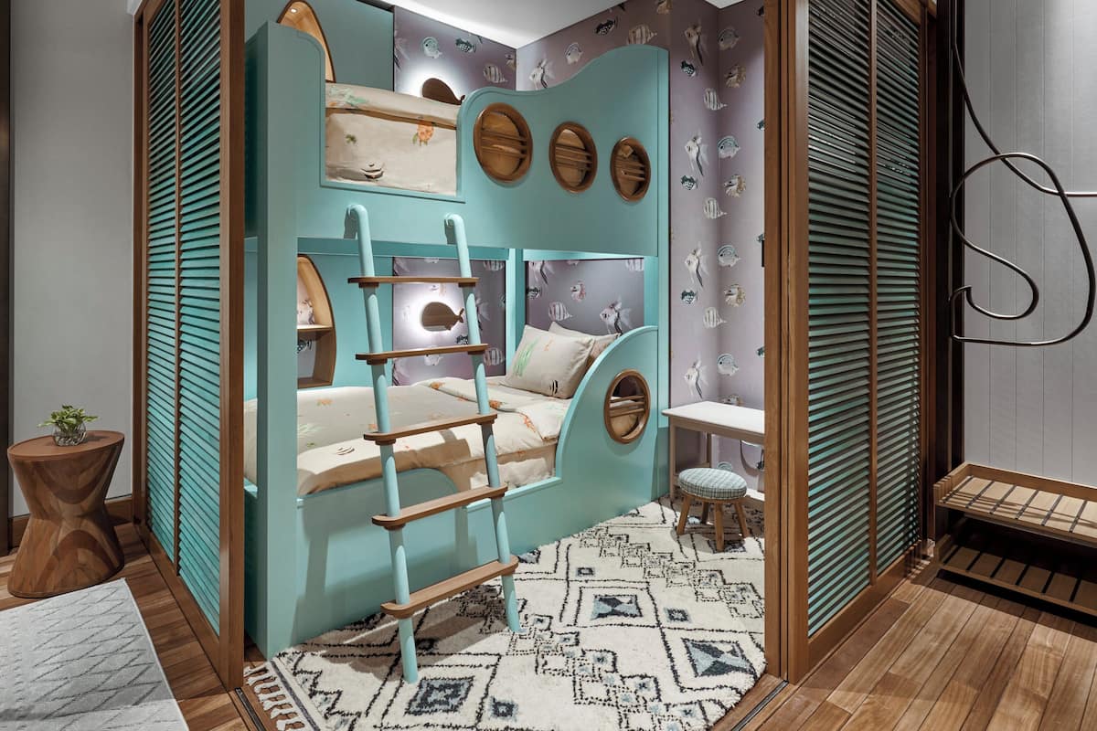 Une pièce avec un lit superposé, un petit tabouret, une plante et un tapis à motifs.