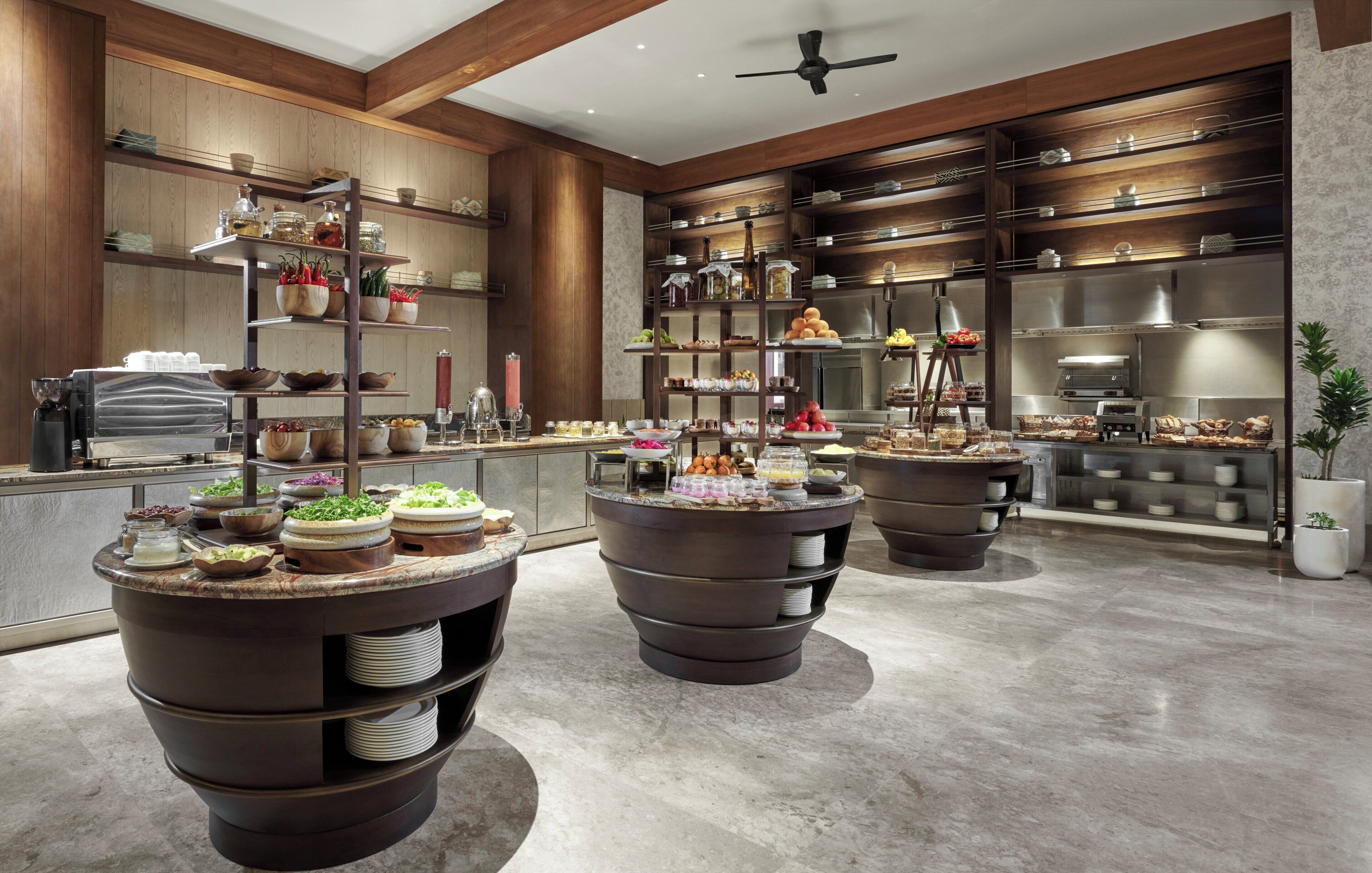A modern kitchen with multiple serving stations, wooden cabinetry, and a variety of food items displayed on shelves and counters.