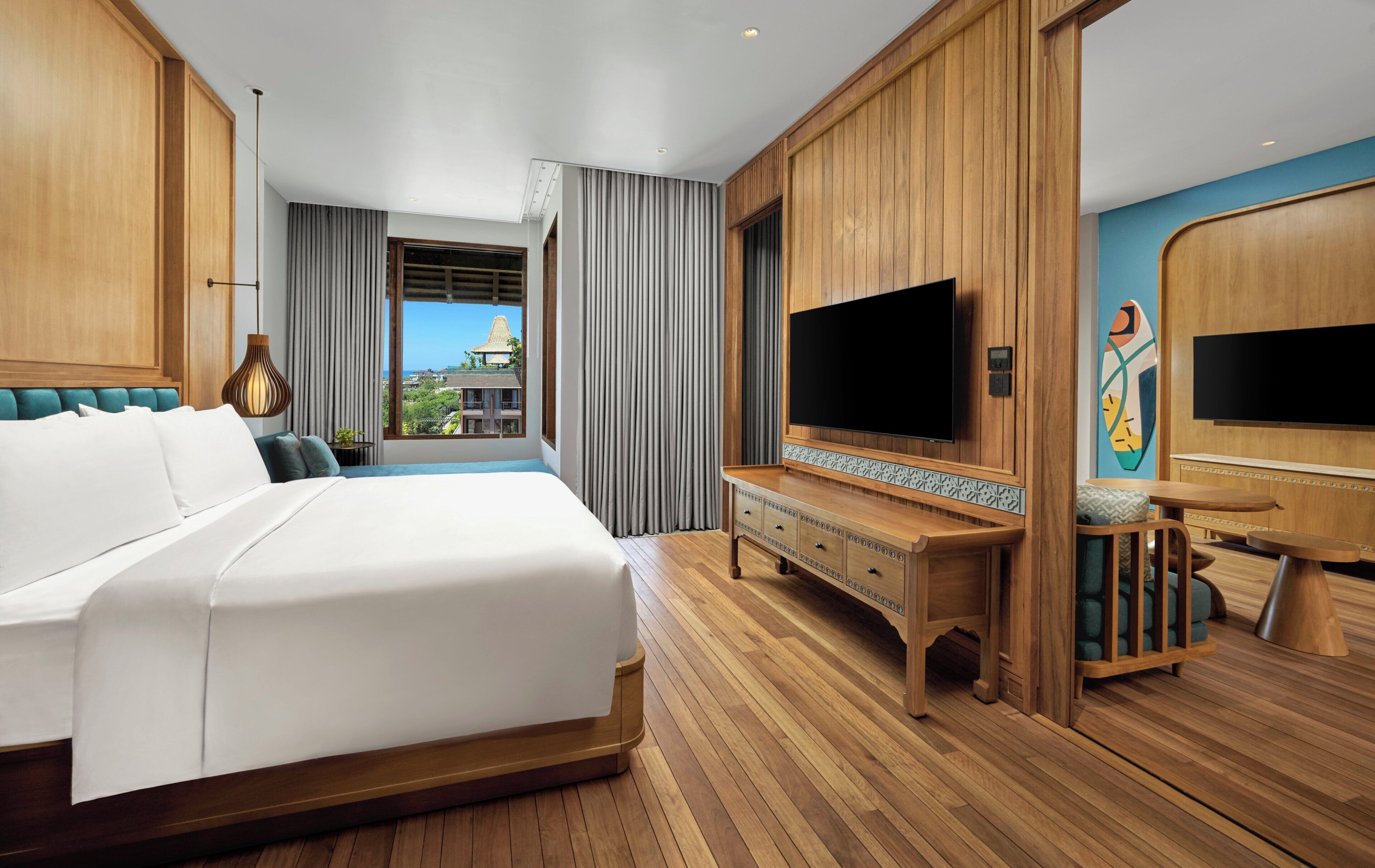 Un cuarto de hotel con una cama grande, un televisor, un aparador de madera y vista al océano.