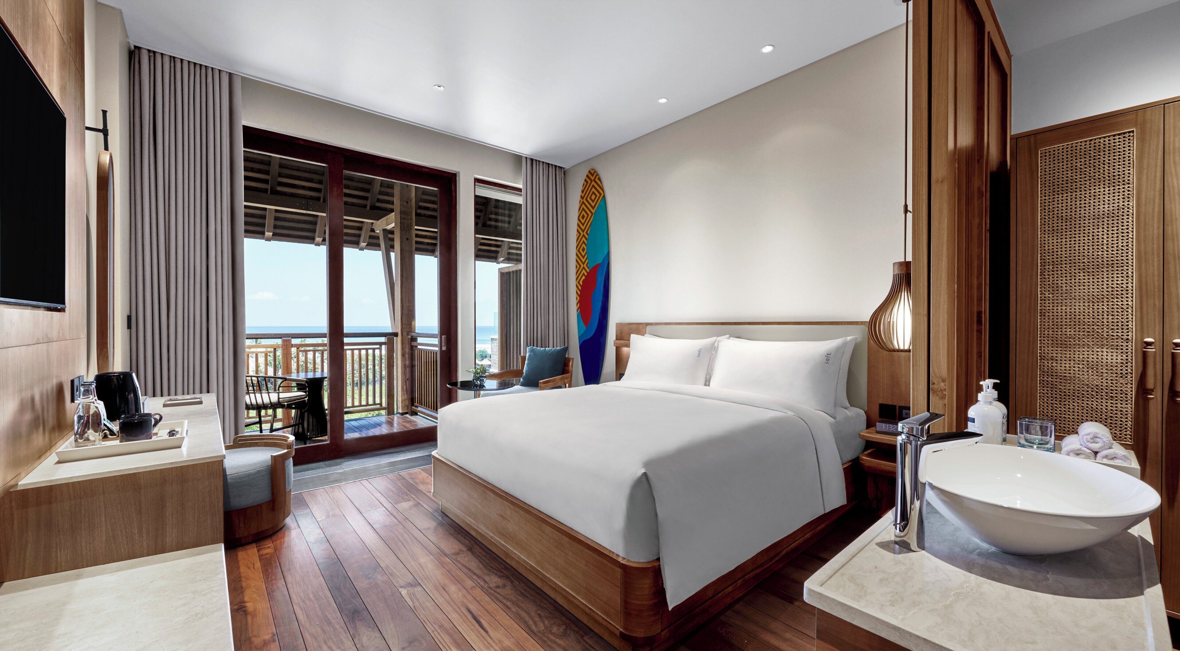 A hotel room with a large bed, a bathroom with a sink and mirror, a coffee station, and a balcony with a view.