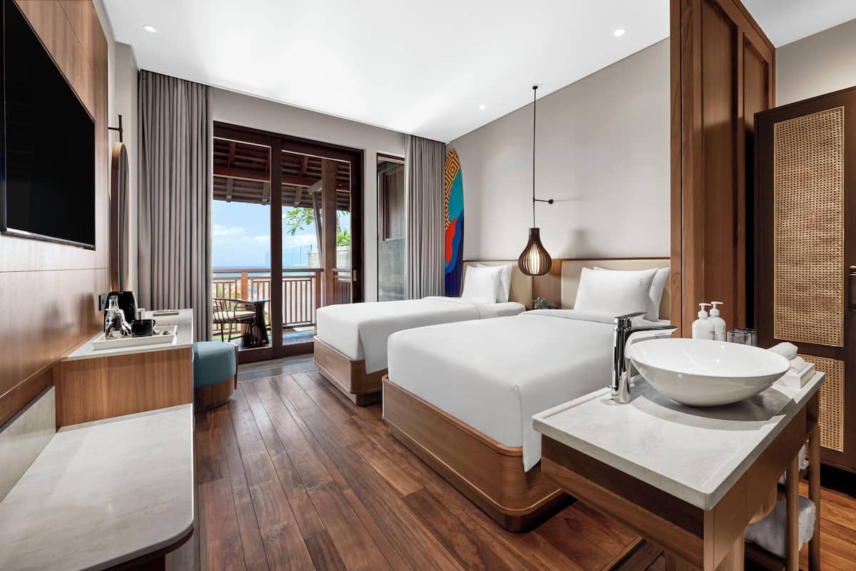 Une chambre d’hôtel avec deux lits, une grande fenêtre, un balcon, un lavabo et une télévision.