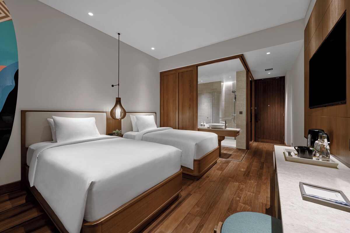 Une chambre d’hôtel avec deux lits, un bureau, un miroir et un espace douche.
