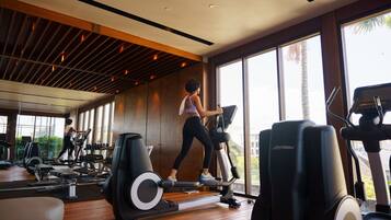 Un gimnasio con equipo de ejercicio diverso, ventanas amplias y techo de madera.