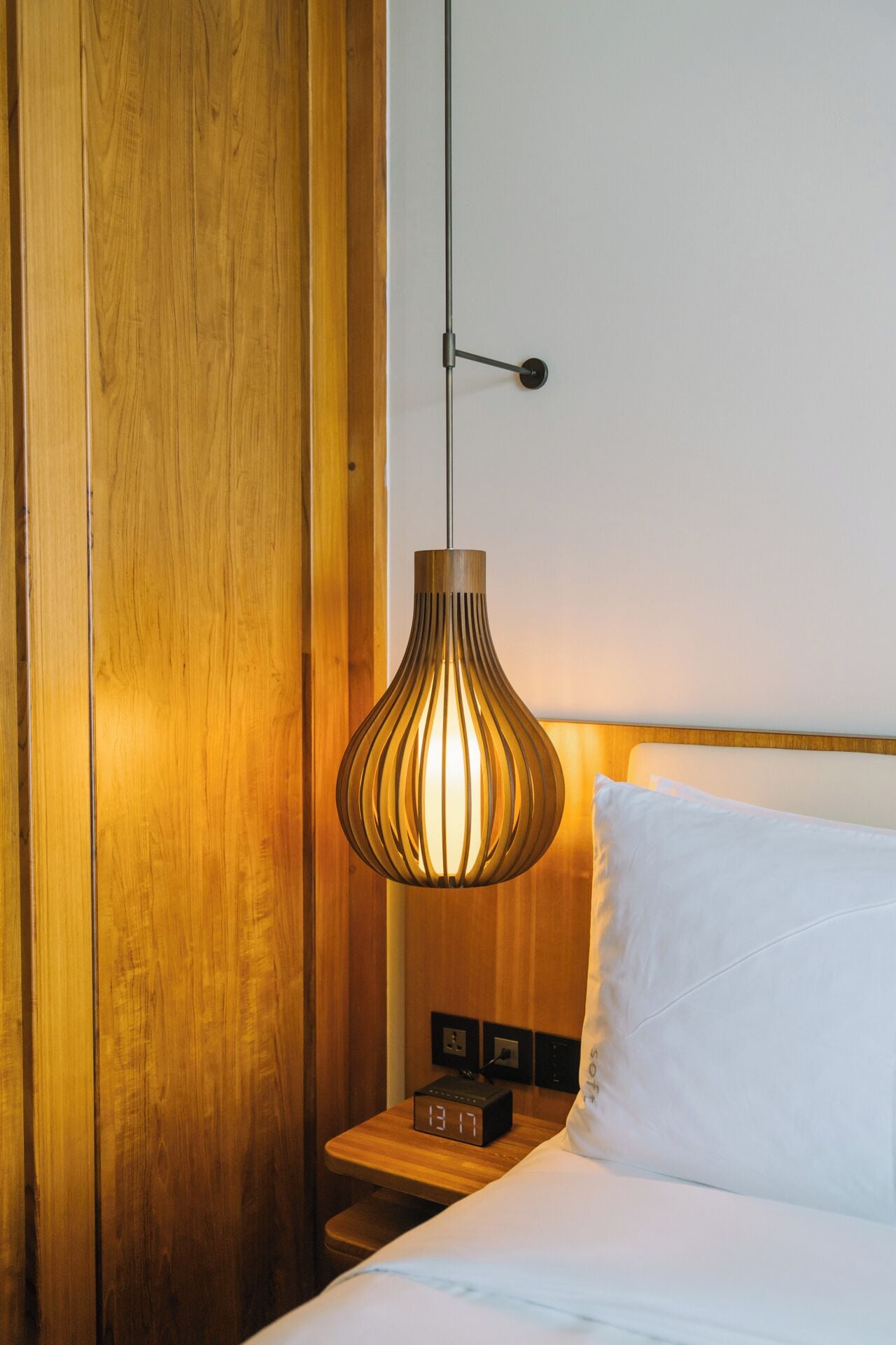 Un armadio in legno, un comodino con una sveglia e una lampada a sospensione in una camera d'hotel.